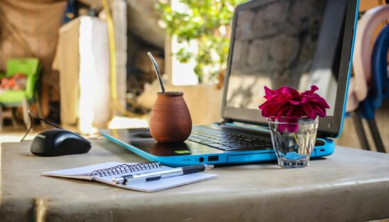 A serene outdoor workspace featuring a laptop, notebook, mug, and flowers on a desk.