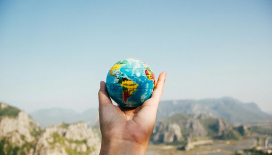 Hand holding a globe against a mountain background symbolizing travel and exploration.