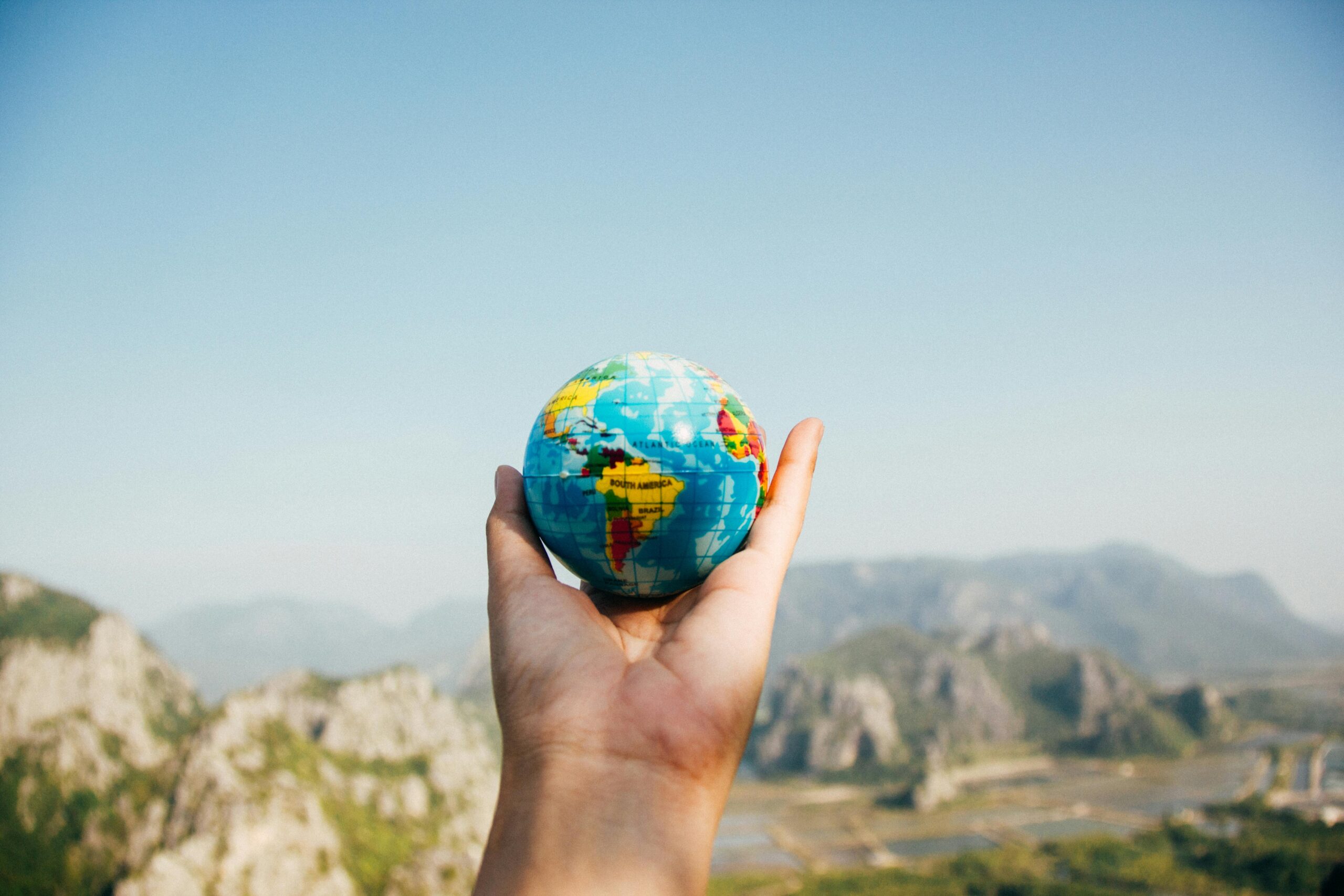 Hand holding a globe against a mountain background symbolizing travel and exploration.