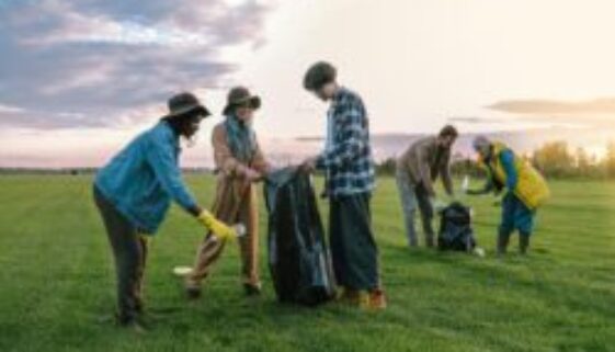 A diverse group of volunteers collecting trash in a field at sunset, promoting environmental awareness.