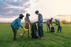 A diverse group of volunteers collecting trash in a field at sunset, promoting environmental awareness.