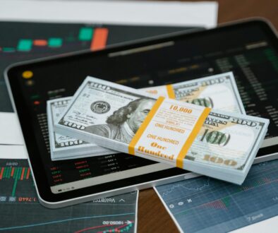 Stack of $100 bills placed on a tablet with financial graphs, symbolizing digital finance.