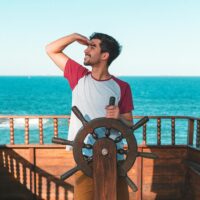 A young man enjoys steering a boat on a sunny summer day at sea, embracing the spirit of adventure.